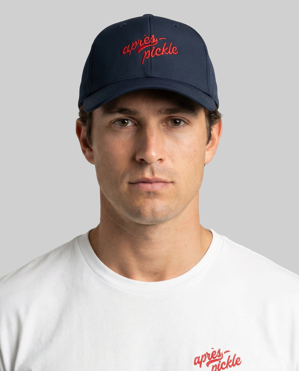 Man wearing a navy cap with red text and a white shirt with red text on a gray background