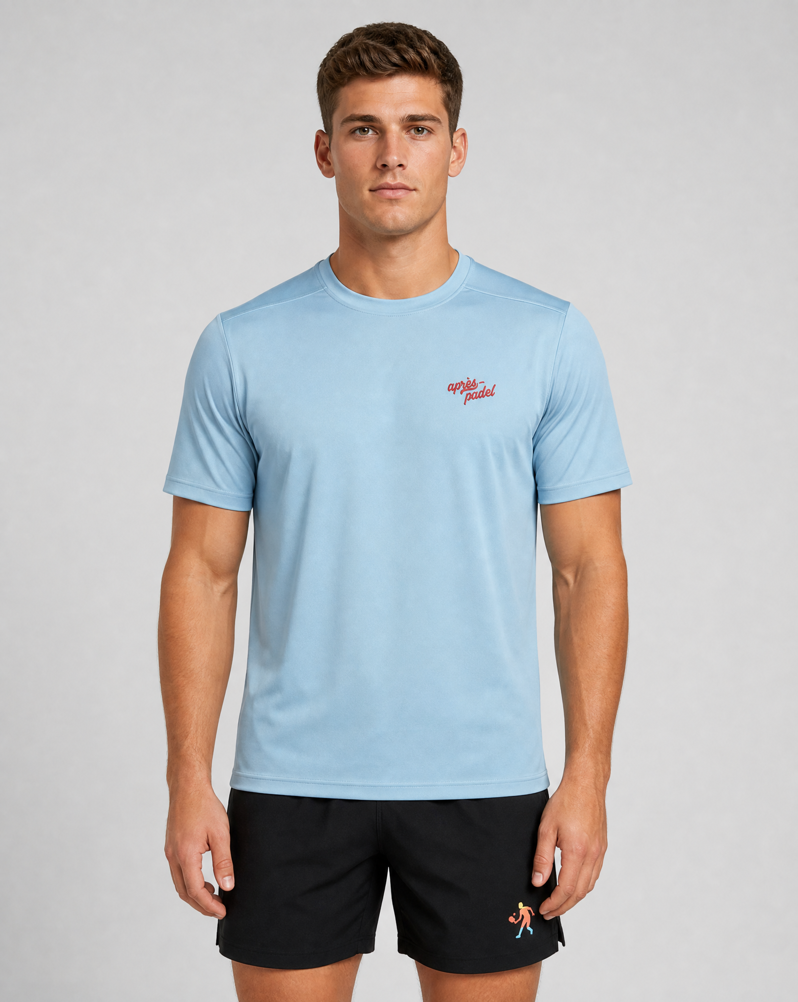 Man wearing a light blue t-shirt with a red logo and black shorts on a gray background